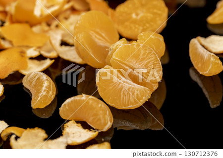 the reflection of an orange tangerine in a mirror surface close up, a peeled and juicy tangerine on a black mirror, close up 130712376