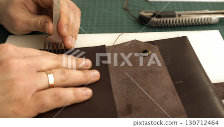 Craftsman using pricking iron tool to punch holes in leather wallet Craftsman using pricking iron tool to punch holes in leather wallet 130712464