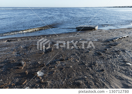 A calm shoreline with visible sand, ice formations, and gentle water waves 130712780