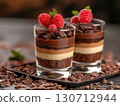 Two elegant dessert glasses display a beautiful arrangement of layered chocolates, featuring rich textures and vibrant raspberries. Perfect for any special occasion or celebration. 130712944
