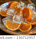 Refreshing slices of orange are artfully arranged with clear ice cubes on a decorative metallic plate, perfect for a warm summer day. The vibrant colors enhance the presentation. 130712957