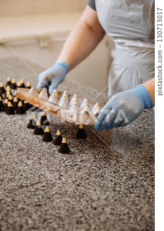 Handmade chocolate candies being unmolded at confectionery factory by chocolatier in gloves Handmade chocolate candies being unmolded at confectionery factory by chocolatier in gloves 130713017