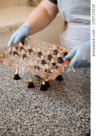 Handmade chocolate candies being unmolded at confectionery factory by chocolatier in gloves 130713019