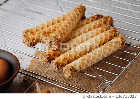 Homemade wafer rolls with nuts on a cooling rack with baking ingredients, rustic setup Homemade wafer rolls with nuts on a cooling rack with baking ingredients, rustic setup 130713028