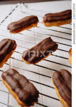 Freshly baked chocolate eclairs cooling on a rack in natural warm light 130713034