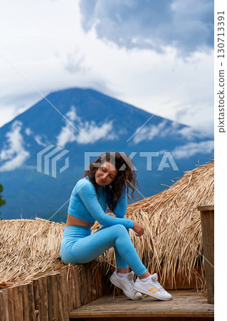 A young woman poses on a large straw photo zone as a bird on a viewing platform and enjoys the view of the sacred Mount Agung volcano hidden by clouds on a rainy day on the island of Bali. A young woman poses on a large straw photo zone as a bird on a viewing platform and enjoys the view of the sacred Mount Agung volcano hidden by clouds on a rainy day on the island of Bali. 130713391