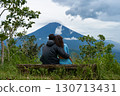 A couple of lovers are sitting on a bench, hugging each other and enjoying the view of the popular sacred cloud-covered Mount Agung on the island of Bali. 130713431
