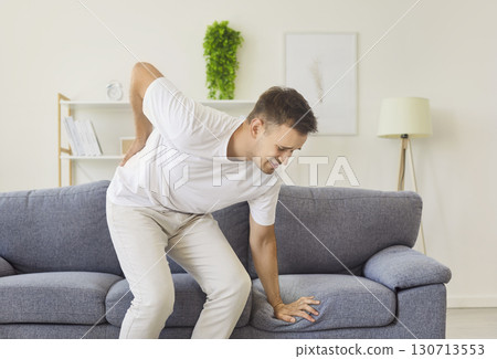Man suffering sharp lower back pain while standing up from couch at home 130713553