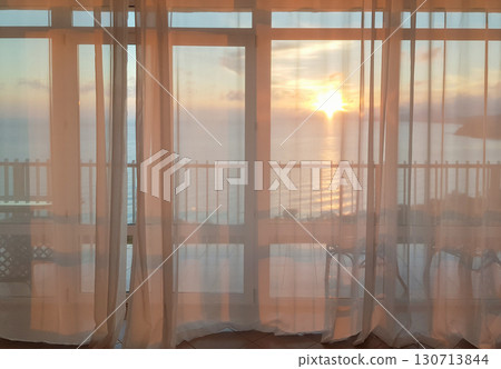 Sunset over the sea through sheer curtains at a balcony panoramic window 130713844