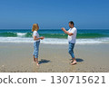 Man photographing woman with a small camera on the beach with waves rolling in and clear blue sky. 130715621