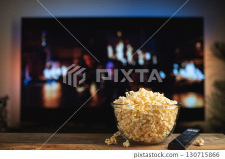 A glass bowl of popcorn and remote control in the background the TV works. Evening cozy watching a movie or TV series at home 130715866