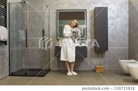 Woman in bathrobe drying hair with towel standing in bathroom interior after taking shower. Woman in bathrobe drying hair with towel standing in bathroom interior after taking shower. 130715918