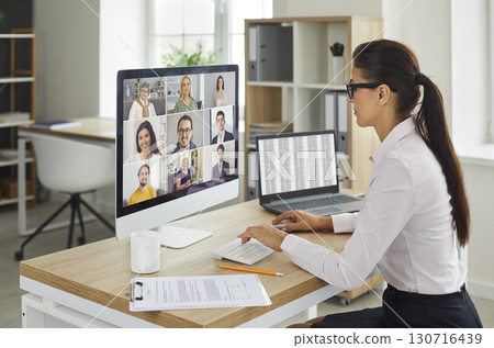 Woman sitting at office desk with computer during remote virtual business team meeting Woman sitting at office desk with computer during remote virtual business team meeting 130716439