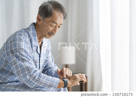 Senior man sitting on bed and operating smartwatch 130718173