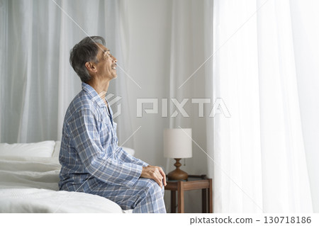 A man in his 60s sitting on a bed 130718186