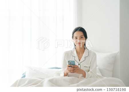 Woman operating smartphone in bed Woman operating smartphone in bed 130718198