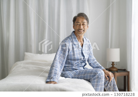 A man in his 60s sitting on a bed looking at the camera and smiling 130718228