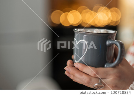 Hands holding a Christmas mug with a heart on the background of a Christmas tree. Bokeh and a festive atmosphere. Love in the family, care and tenderness. High quality photo Hands holding a Christmas mug with a heart on the background of a Christmas tree. Bokeh and a festive atmosphere. Love in the family, care and tenderness. High quality photo 130718884