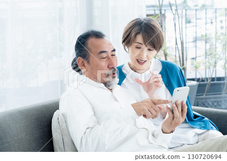 Senior couple looking at smartphone on sofa Senior couple looking at smartphone on sofa 130720694