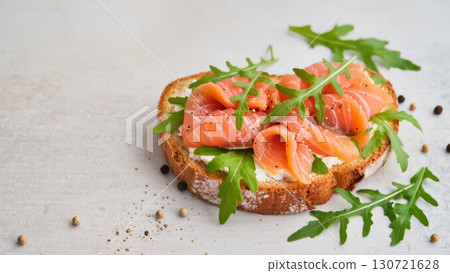 Open sandwich with smoked salmon, cream cheese, arugula, and pepper on crusty bread. Tasty fresh snack on light background. Top view. Open sandwich with smoked salmon, cream cheese, arugula, and pepper on crusty bread. Tasty fresh snack on light background. Top view. 130721628