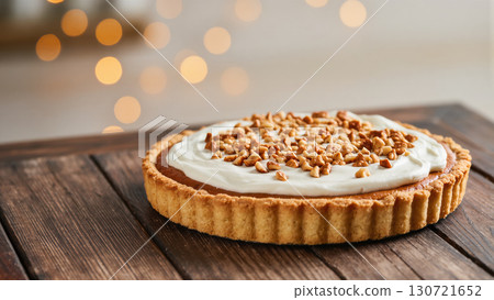 Christmas pie with whipped cream and chopped nuts on top, served on rustic wooden table with festive blurred lights 130721652