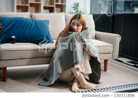Young Asian woman suffering from flu symptoms, covered with a blanket on a sofa. Concept of illness, healthcare, and recovery. 130721886