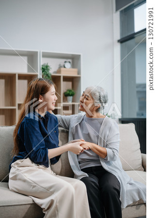 Happy adult Asian granddaughter and senior grandmother having fun enjoying talk sit on sofa in living room using a laptop, tablet 130721991