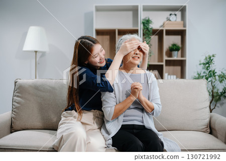 Happy adult Asian granddaughter and senior grandmother having fun enjoying talk sit on sofa in living room using a laptop, tablet 130721992