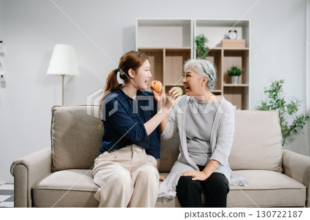 Happy adult Asian granddaughter and senior grandmother having fun enjoying talk sit on sofa in modern living room, using a laptop, tablet 130722187