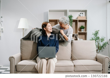 Happy adult Asian granddaughter and senior grandmother having fun enjoying talk sit on sofa in modern living room, using a laptop, tablet 130722188