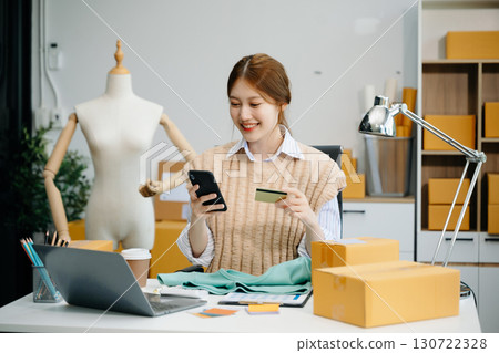 Young woman running online store Startup small business SME, using smartphone or tablet taking receive and checking 130722328