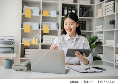 Young beautiful woman typing on tablet and laptop while sitting at the working wooden table office Young beautiful woman typing on tablet and laptop while sitting at the working wooden table office 130722338