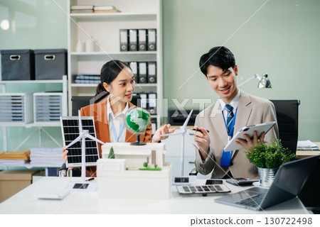Young professionals for a greener future. Showcasing renewable energy solutions with solar panels, wind turbines, and a model house. 130722498