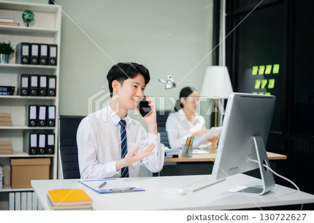 Two young Asian professionals engaged in teamwork and business discussions in modern office embodying corporate Two young Asian professionals engaged in teamwork and business discussions in modern office embodying corporate 130722627