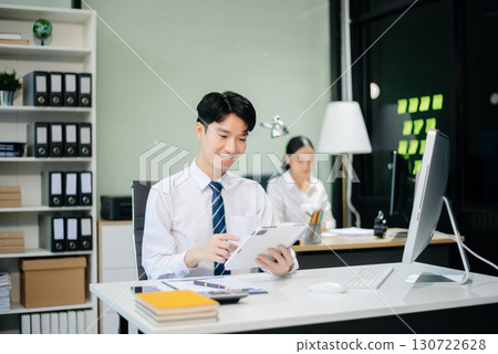 Two young Asian professionals engaged in teamwork and business discussions in modern office embodying corporate 130722628
