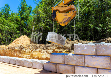 Crew installs concrete blocks at site surrounded by tall trees during construct newly retaining wall 130723492