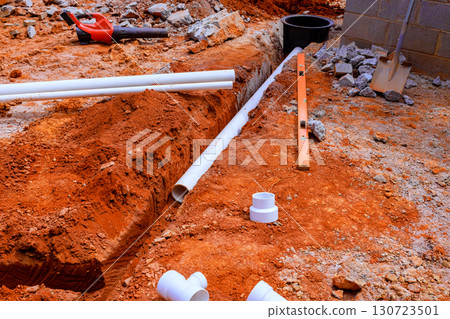 Workers prepare trenching for plumbing by laying pipes in trench at suburban construction site. 130723501