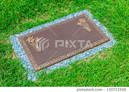 Bronze memorial marker with floral engravings cross rests on peaceful cemetery 130723509