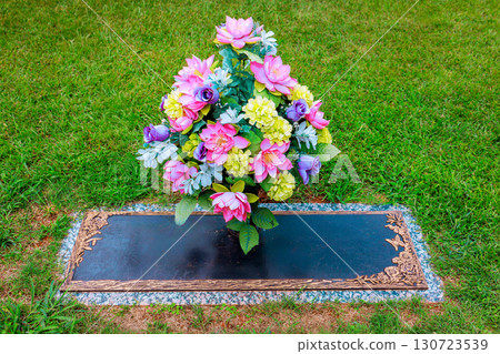 Artificial flowers display vibrant colors at grave marker, creating peaceful tribute in well kept cemetery. 130723539