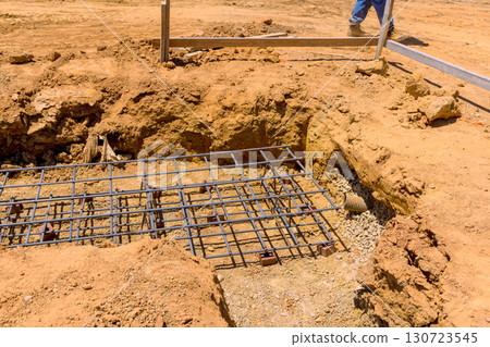 Construction workers engage in laying foundation with rebar freshly excavated soil at under construction work day 130723545