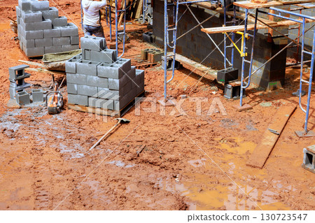 Workers are constructing walls using concrete blocks while navigating muddy construction site under works day Workers are constructing walls using concrete blocks while navigating muddy construction site under works day 130723547