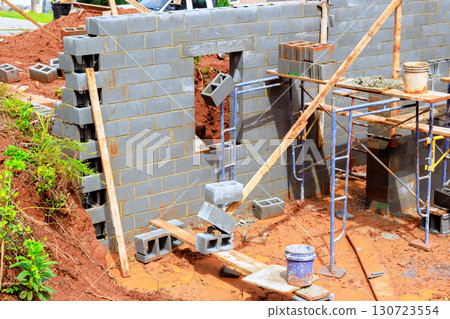 Workers lay blocks for new structure while using scaffolding, tools at construction site during works day. Workers lay blocks for new structure while using scaffolding, tools at construction site during works day. 130723554