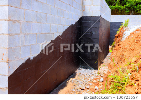 Workers apply black waterproofing paint to foundation walls in preparation for construction at residential site. 130723557