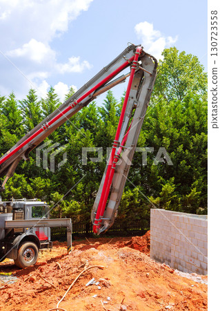 Concrete pump truck delivers concrete to wall being built at construction site on work day 130723558