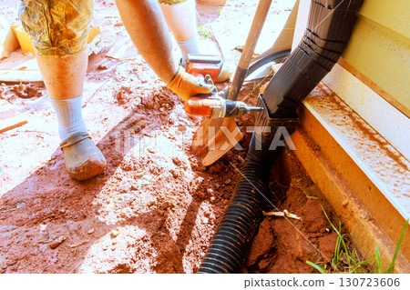 Person uses drill to connect parts of drainage system in garden area. 130723606