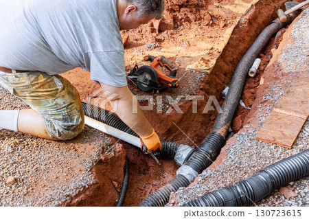 Worker lays drainage pipes in trench at home construction site as part of ground preparation for plumbing. 130723615