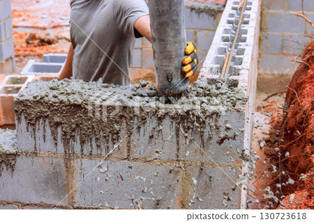 Construction worker skillfully fills concrete into blocks while building structure on works day outdoors. 130723618