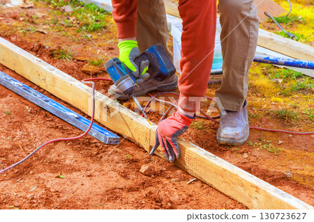Worker skillfully fastens wooden beams with cordless drill on construction site during works day hours. Worker skillfully fastens wooden beams with cordless drill on construction site during works day hours. 130723627