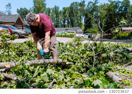 Contractor uses chainsaw to cut logs branches in yard after thunder strong storm 130723637