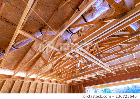 Workers are installing wooden roof frame in new house, showcasing structural components building progress. 130723646